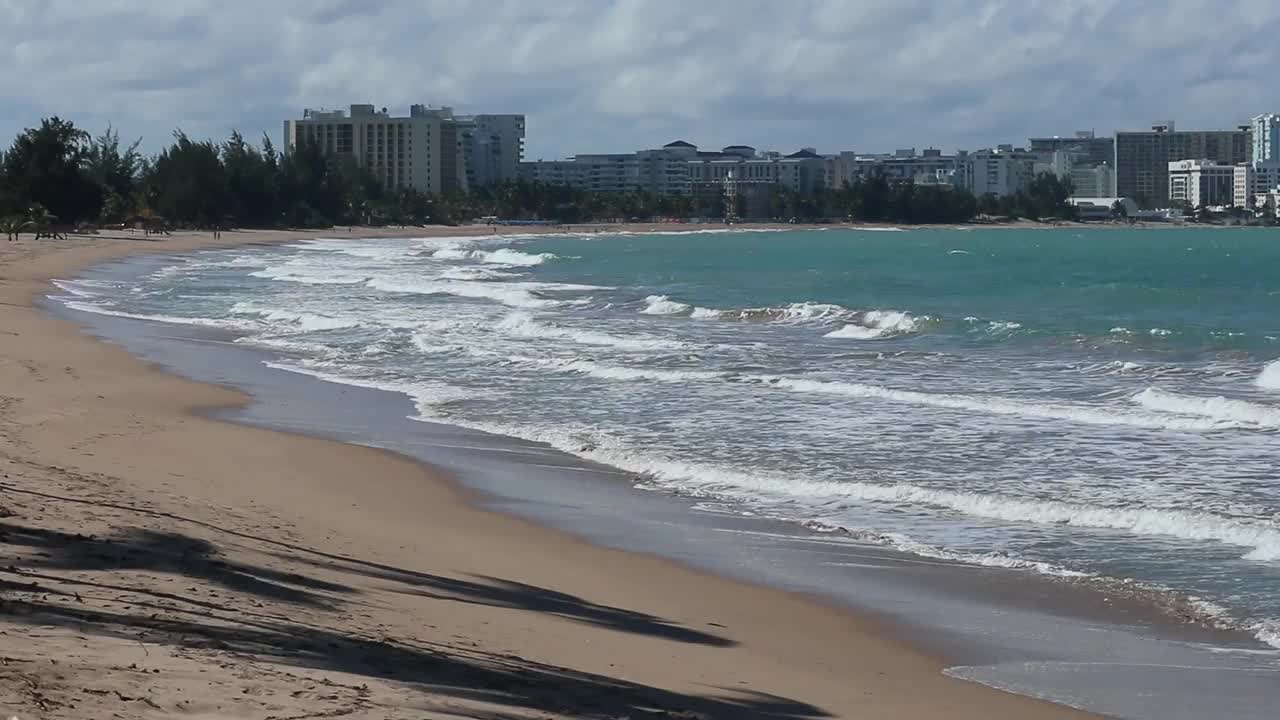 卡罗莱纳海滩海岸与远处的高层酒店和住宅建筑在波多黎各(加勒比海岛屿旅游度假度假)田园诗般的宁静天堂冲浪水沙波圣胡安视频下载