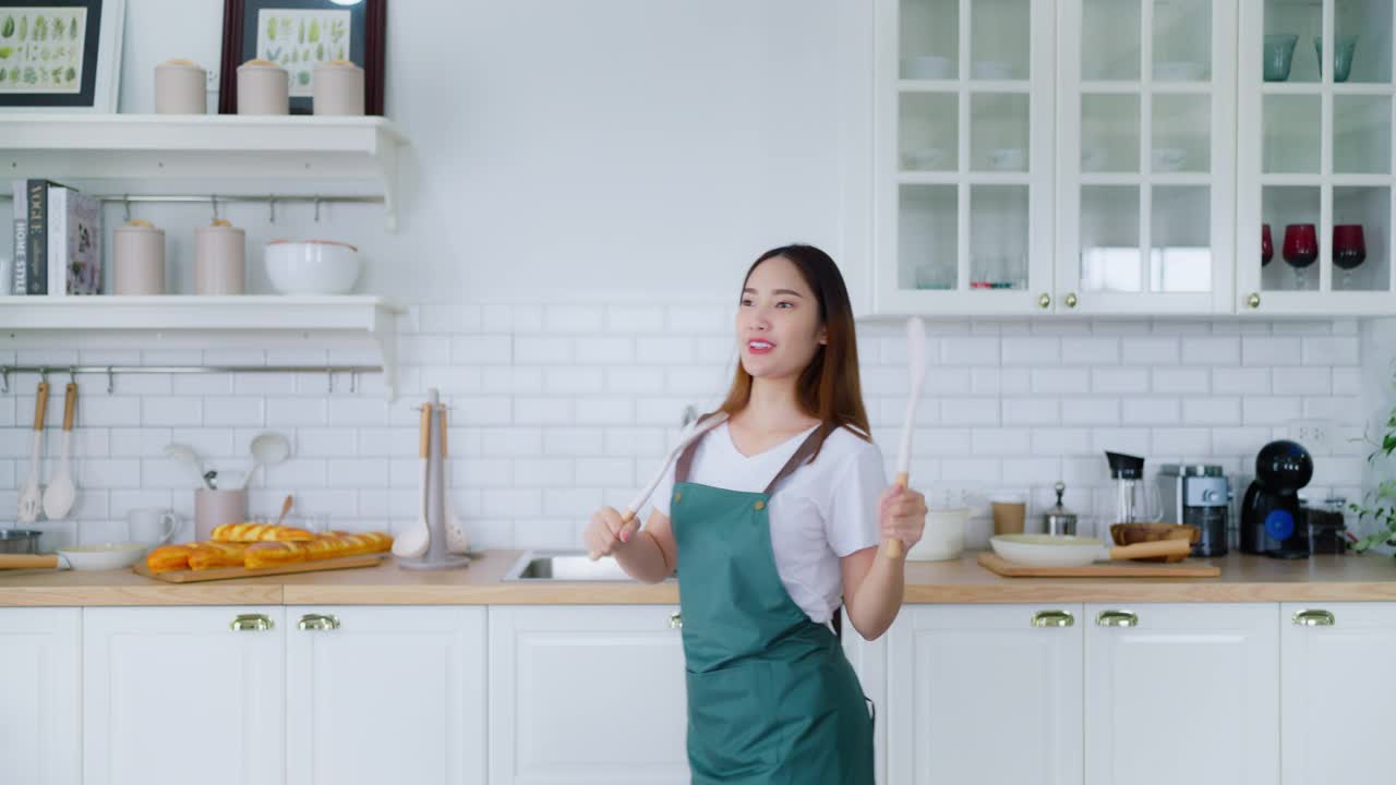 年轻的亚洲女人在厨房里跳舞。一个美丽的女人在周末的空闲时间在家里放松的快乐视频下载