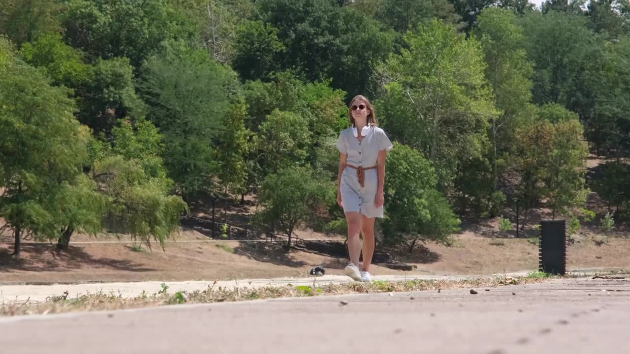 夏日的午后，一位快乐的年轻女子正走在城市公园的中心，听着音乐视频下载