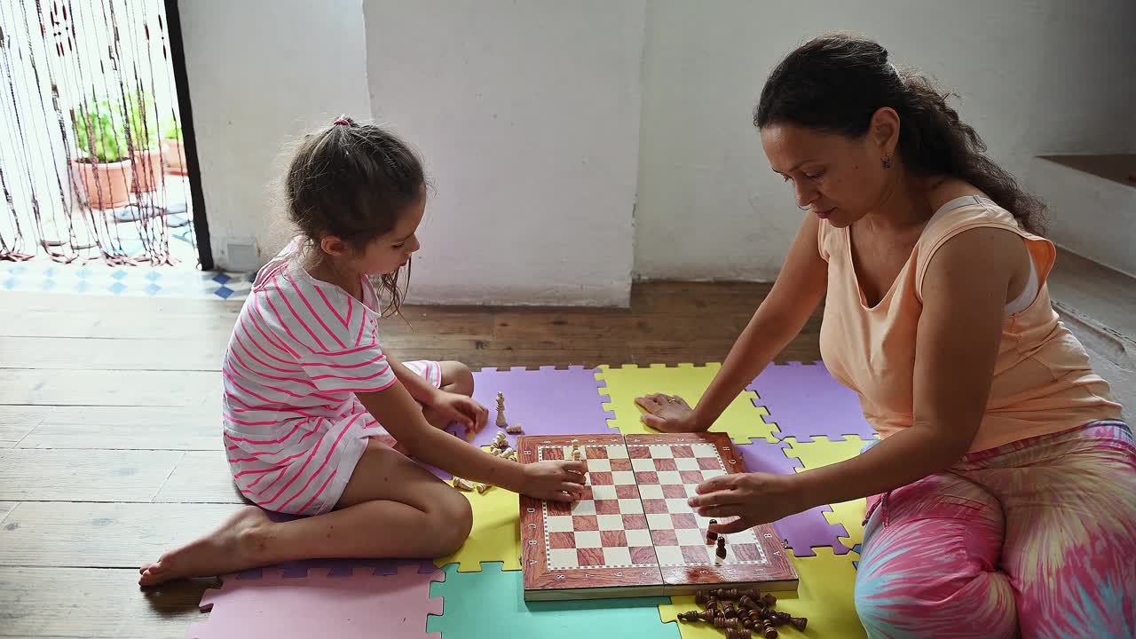 母女俩在舒适的家庭环境中，在五颜六色的泡沫垫子上下棋，在轻松的环境中展示家庭关系和战略思维。视频素材