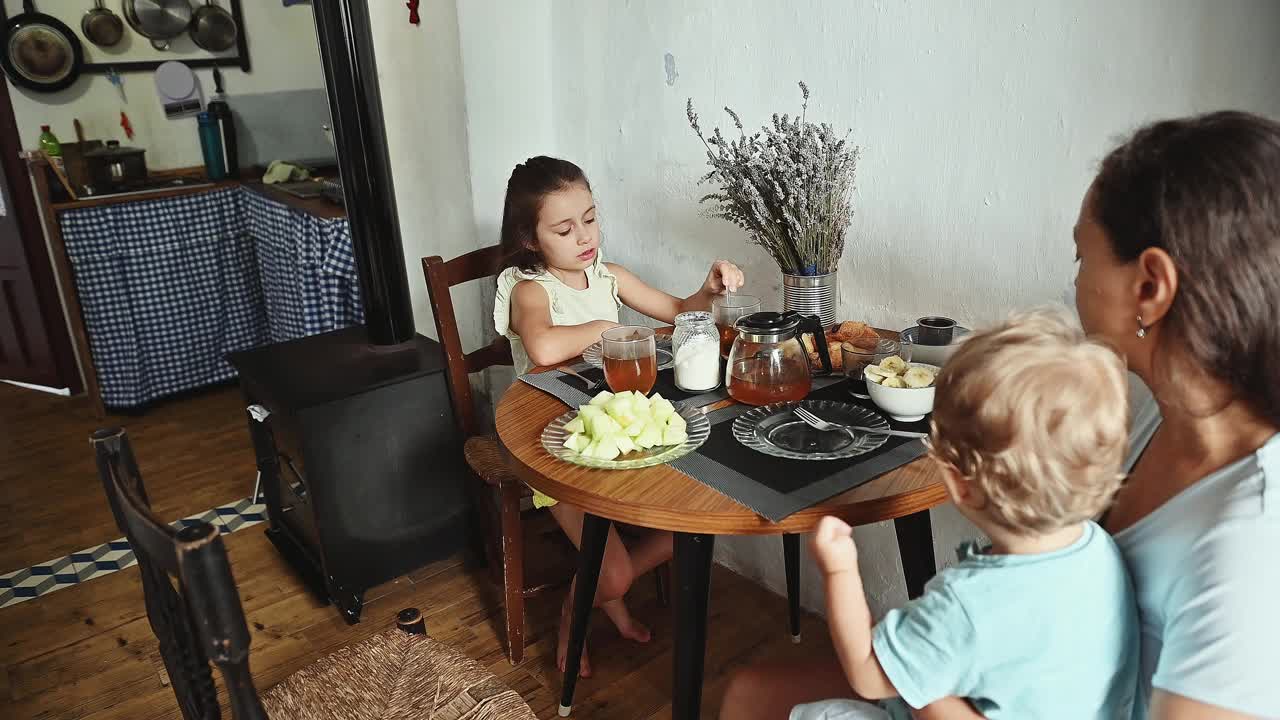 一家人一起在家里享用早餐，品尝新鲜的水果、茶和温暖舒适的氛围。孩子和母亲在轻松的早餐中分享美好时光。视频素材