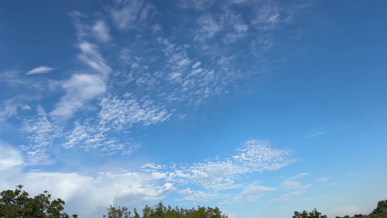 蓝天上的高积云和前景阳光下的树木视频下载