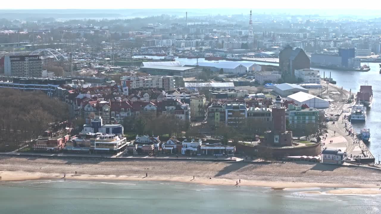 无人机拍摄了Kołobrzeg海港，突出了灯塔、建筑物和远处的游艇码头。视频下载