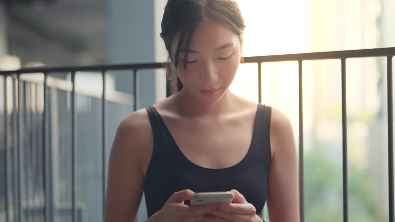 穿着黑色运动服的亚洲女性在城市中使用手机，女性在智能手机的移动应用程序中查看脉搏或比赛时间视频下载