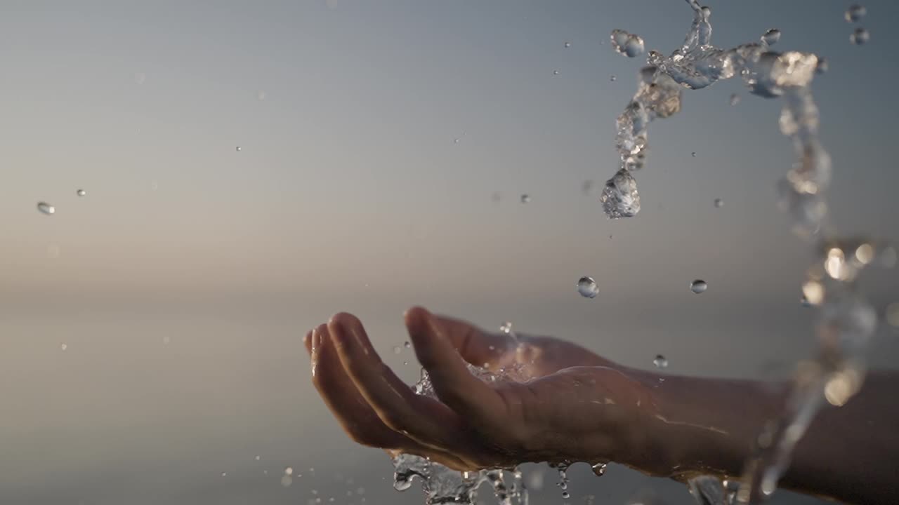 温柔的水从手流动在夕阳的背景视频下载