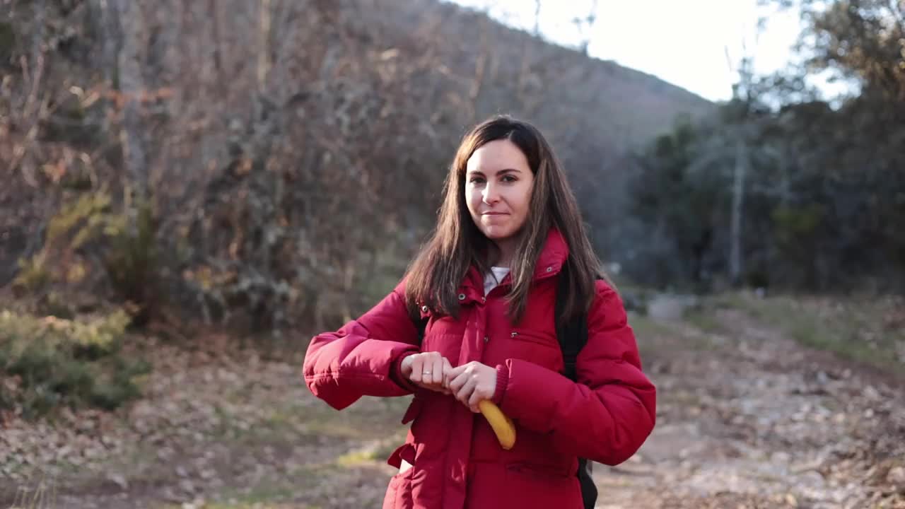 徒步旅行后在森林里剥香蕉的漂亮女人。她没有削皮，笑了。视频下载