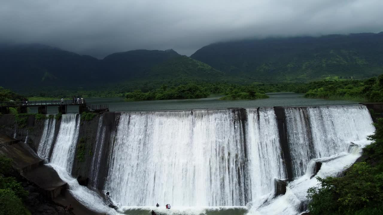 丰沛的水——马哈拉施特拉邦莱加德邦潘维尔莫尔贝村的一座小水坝，在季风期间，在美丽的山丘、绿色的森林和云层的衬托下，大坝溢流。视频下载