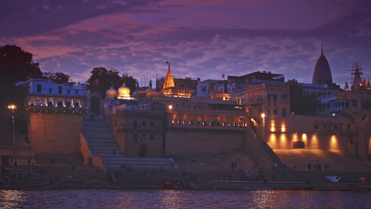 印度瓦拉纳西。游客和朝圣者走过Janaki Ghat。摄像机沿着河岸堤岸移动。晚上在神圣的瓦拉纳西高山上。傍晚时分的紫色日落天空视频下载