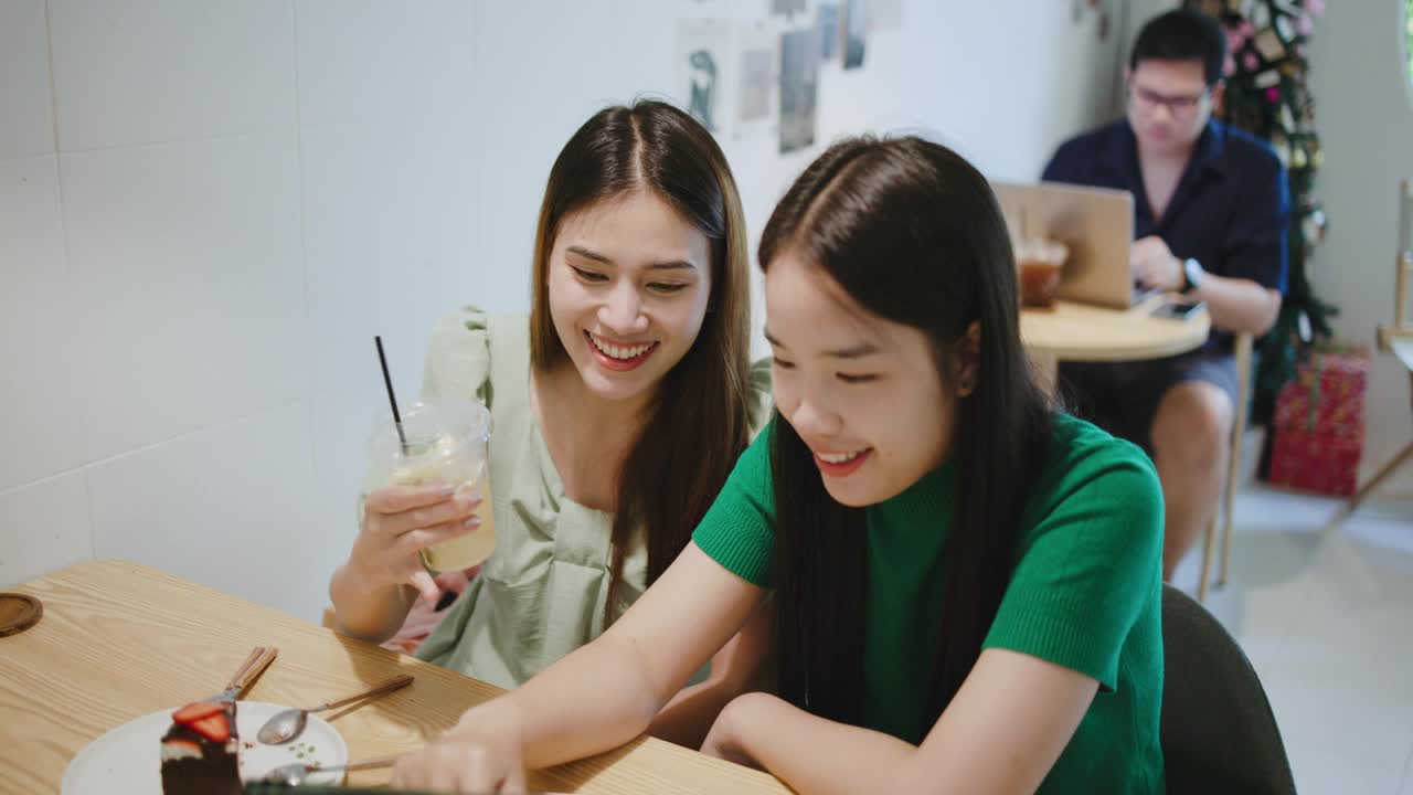 咖啡店里，两个漂亮的年轻女子正在一块平板电脑上玩游戏。视频下载