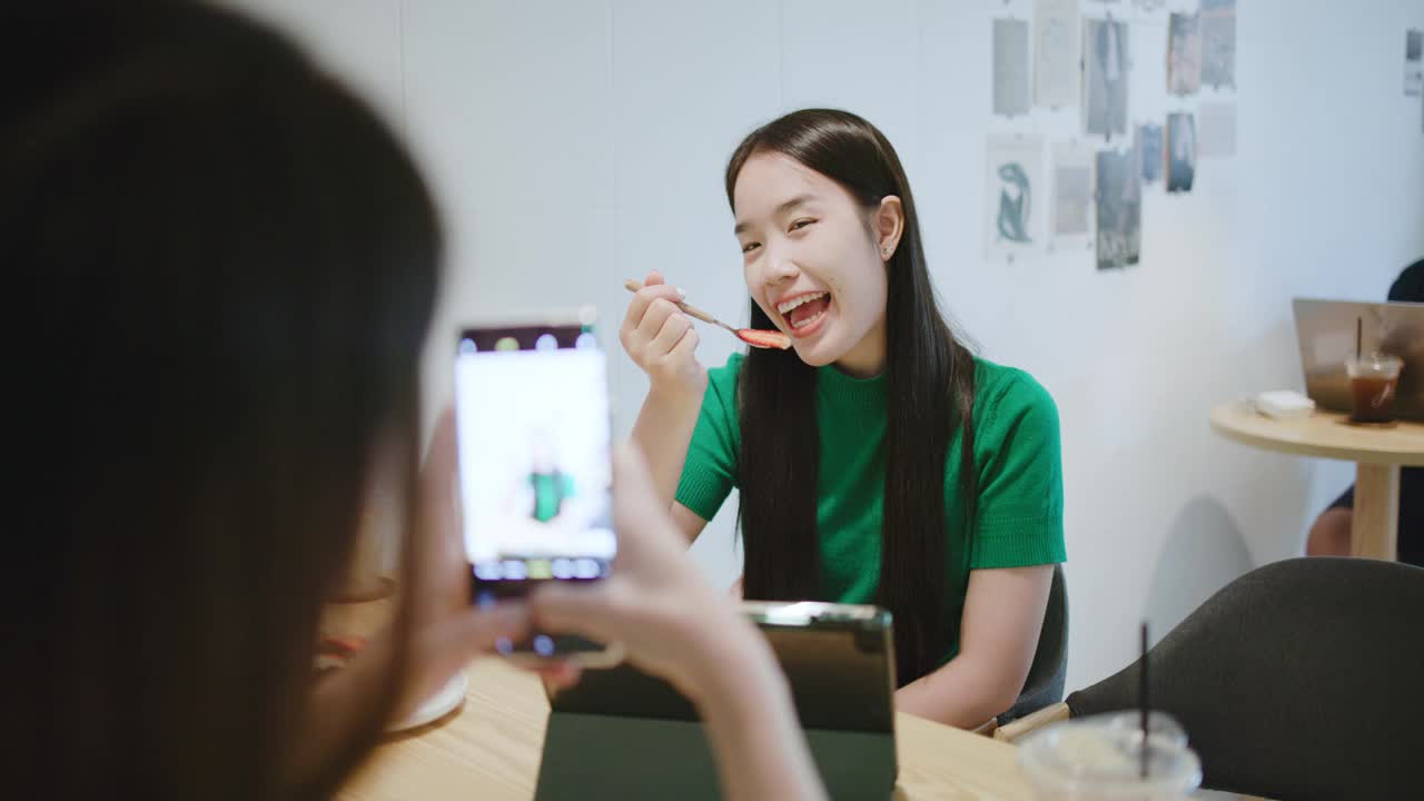 两个快乐的年轻女子在咖啡店用智能手机互相拍照。视频下载