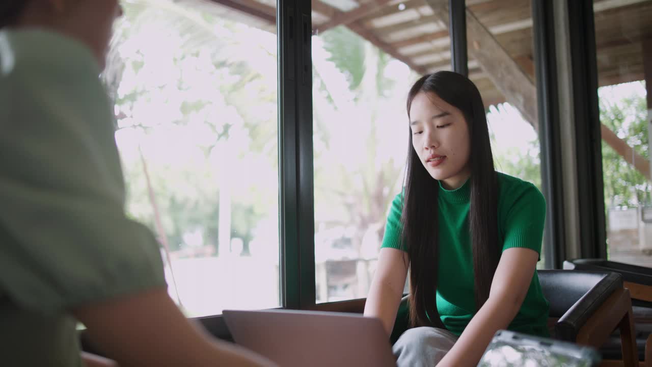 两位年轻女性在咖啡店用笔记本电脑讨论项目或想法。视频下载