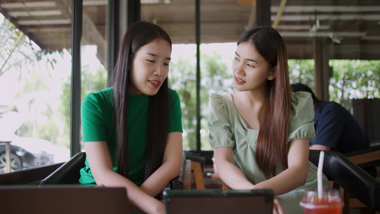 两位年轻女性在咖啡店用笔记本电脑讨论项目或想法。视频素材