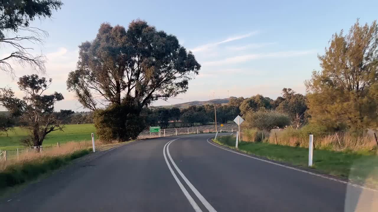 一辆汽车行驶在乡间的单车道公路上，穿过树林蜿蜒前行，窗外的景色视频下载