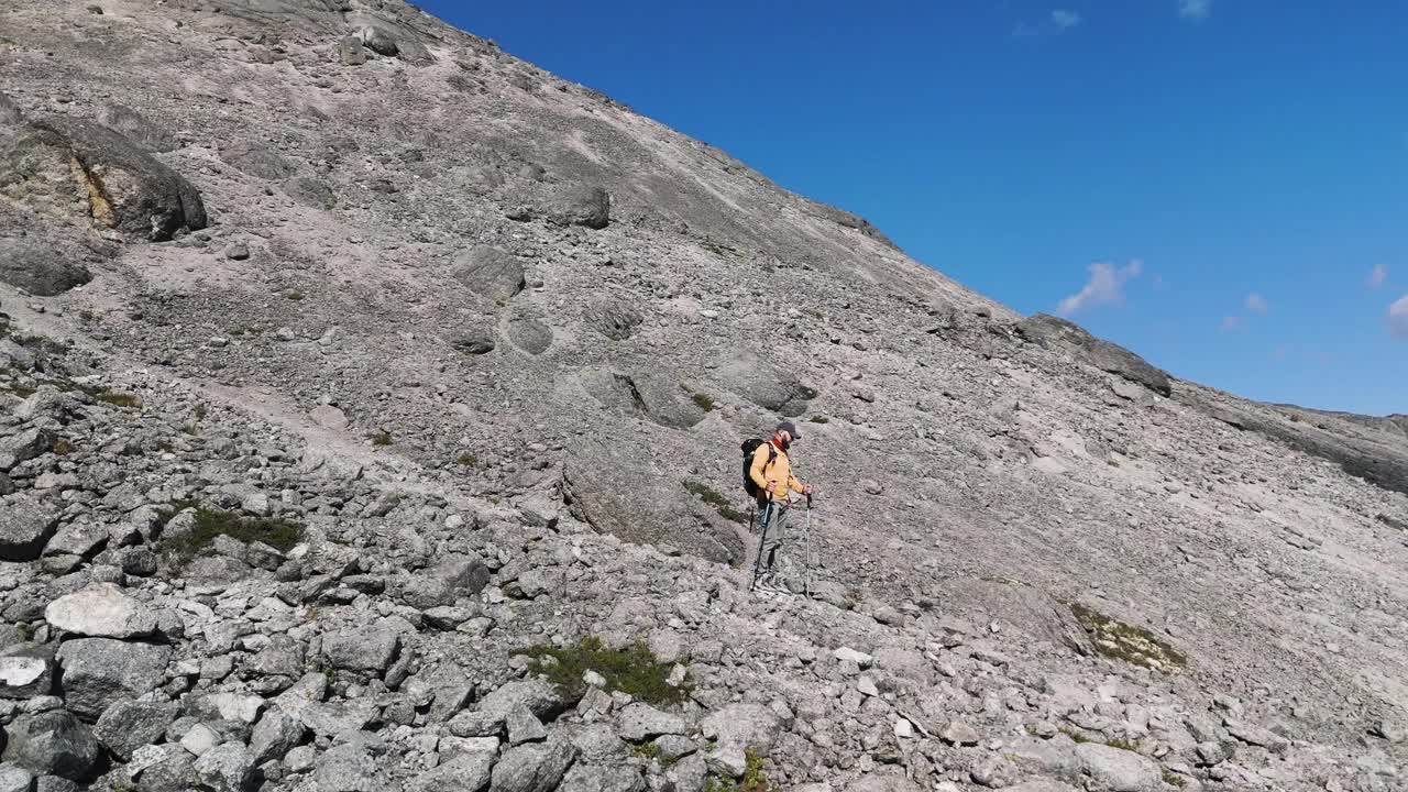 徒步旅行者背着背包和登山杖站在岩石嶙峋的山坡上视频下载