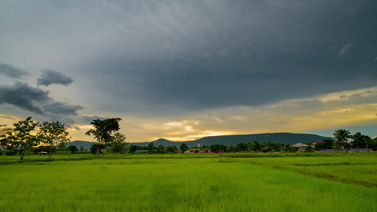 夕阳多云的天空下，一片宁静的绿色田野，地平线上有树木和远山。视频素材