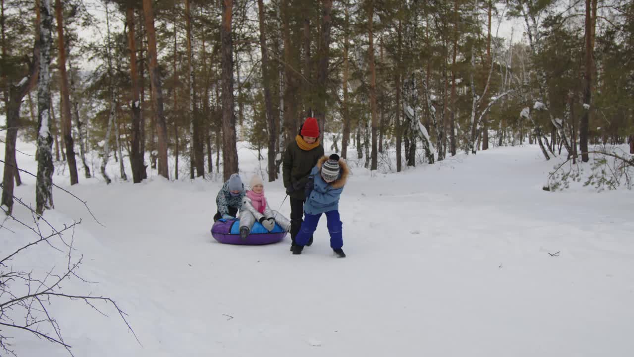 孩子们用充气雪撬拉着小女孩上山视频素材