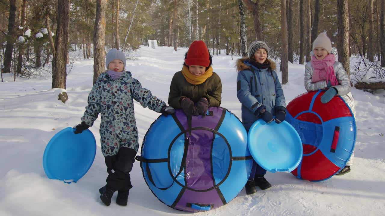 森林里快乐的男孩和女孩拿着雪管和雪碟的肖像视频下载