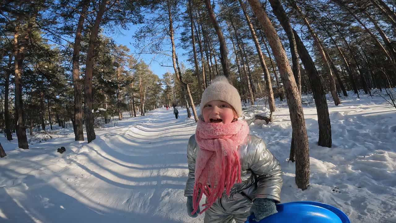 和顽皮的女孩在森林里散步，骑着雪盘下山的镜头视频下载