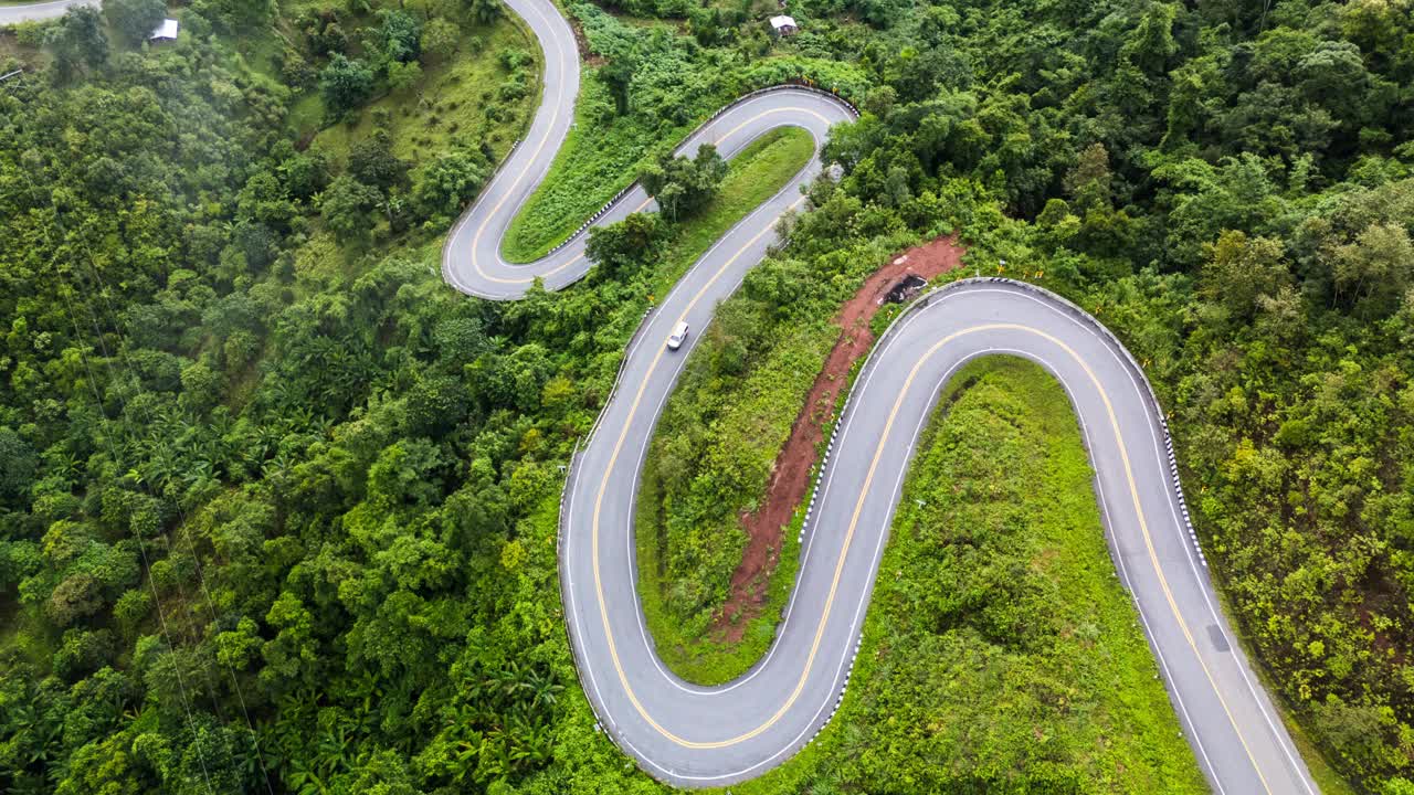 弯弯曲曲的道路蜿蜒穿过茂密的绿色森林。视频下载