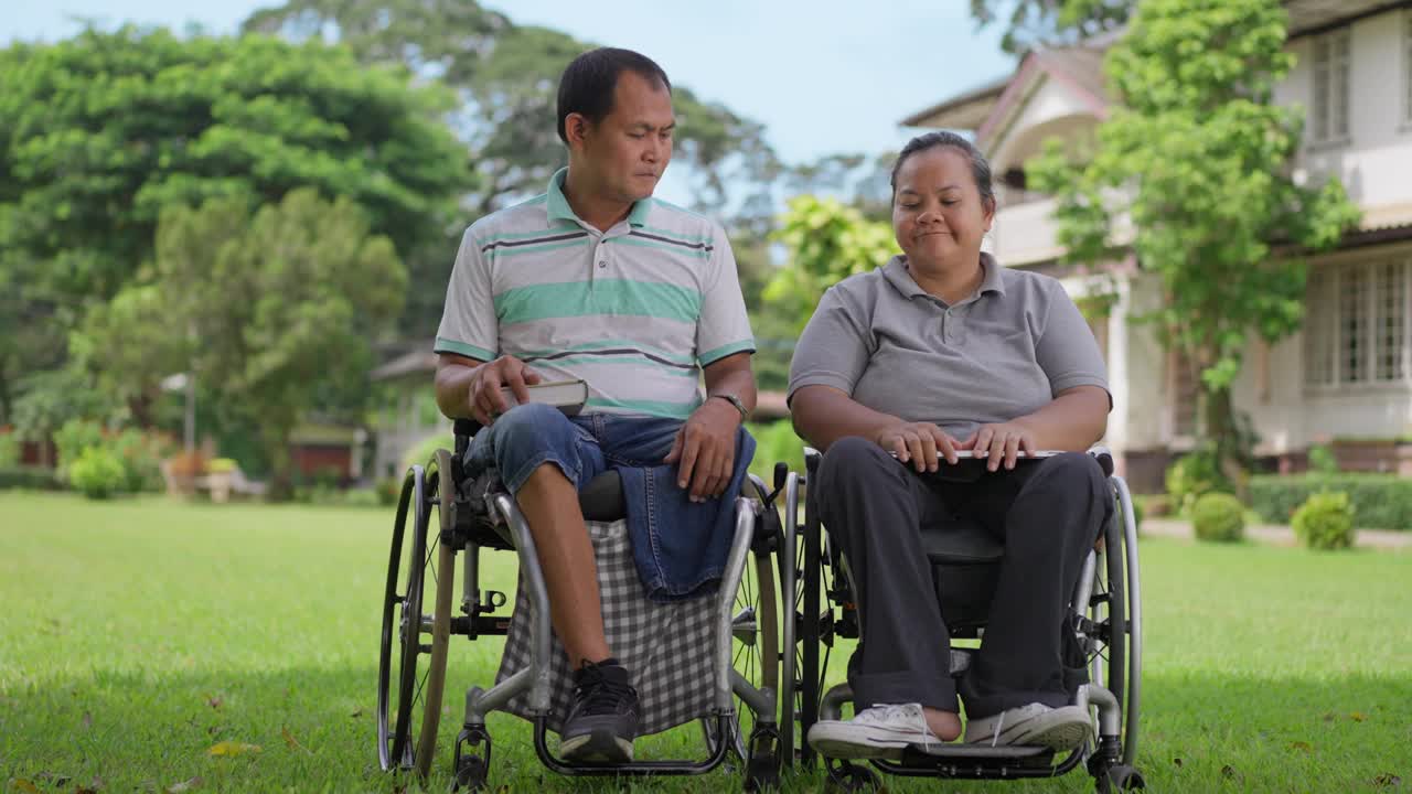 幸福的轮椅使用者夫妇享受彼此的陪伴，一起呆在外面，丈夫俯身给妻子一个吻。视频下载