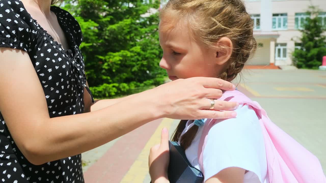 快乐的妈妈送漂亮的小女儿去小学，抱着爱的户外特写。在校园操场上，微笑的年轻女子拥抱小学生视频下载