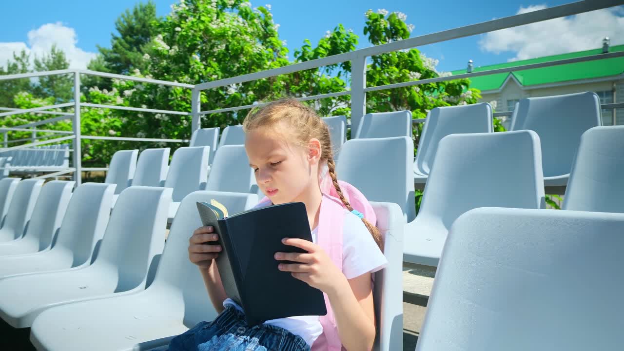 女学生，小学生，小学生，小女孩放学后坐在操场外面的街道上拿着书和笔记本视频素材