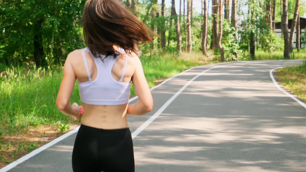 年轻女子在公园慢跑。身穿运动服的黑发女郎喜欢在森林里户外跑步视频下载