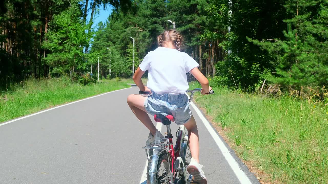 小女孩在森林里骑自行车。孩子在路上骑自行车，近距离在户外玩耍。合家休闲，节假日活跃，童年。视频下载