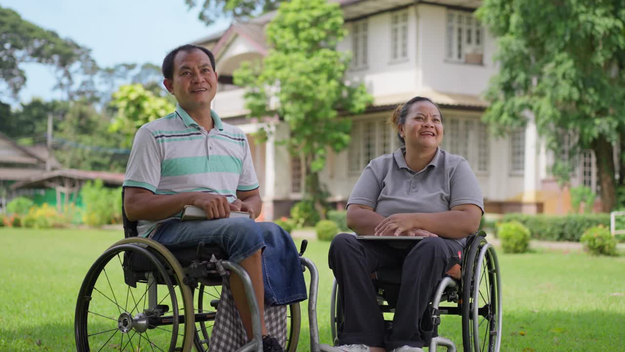 幸福的轮椅使用者夫妇，丈夫和妻子，享受着彼此的陪伴，微笑和笑声，在一个阳光明媚的日子里在外面放松视频下载