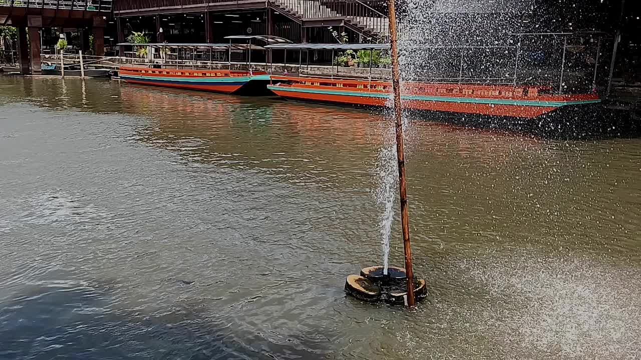 运河里的一个小喷泉，背景是一艘长尾船。视频下载