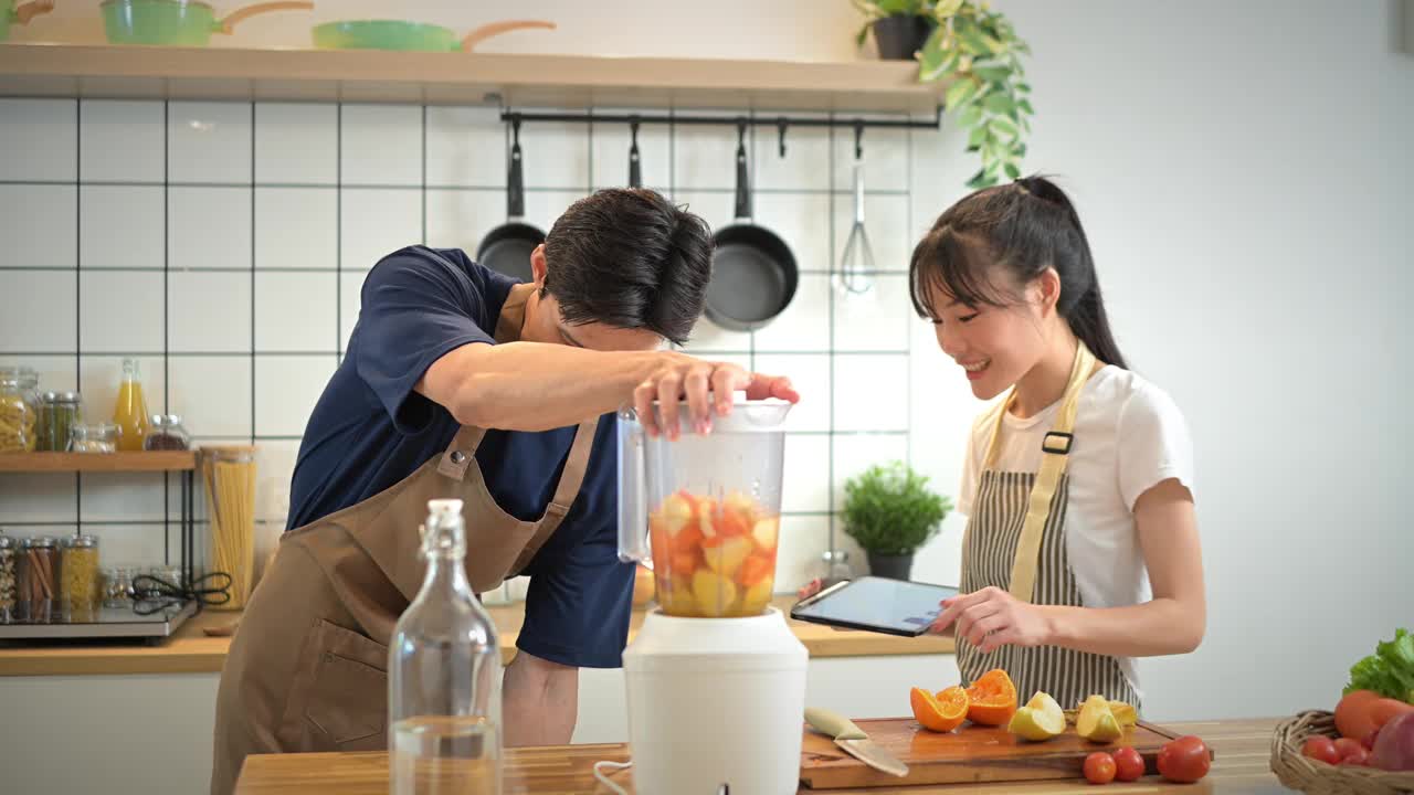 可爱的年轻夫妇享受烹饪课程一起准备新鲜的冰沙或果汁在厨房。视频素材