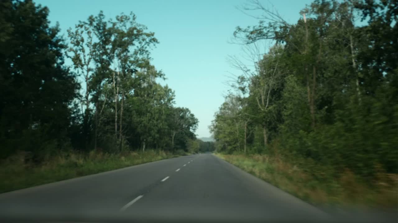 在温暖的阳光明媚的日子里，汽车行驶在夏季或秋季森林附近的道路上，在冒险和新体验的路上，活跃的年轻人的生活方式。旅行和冒险的概念视频下载