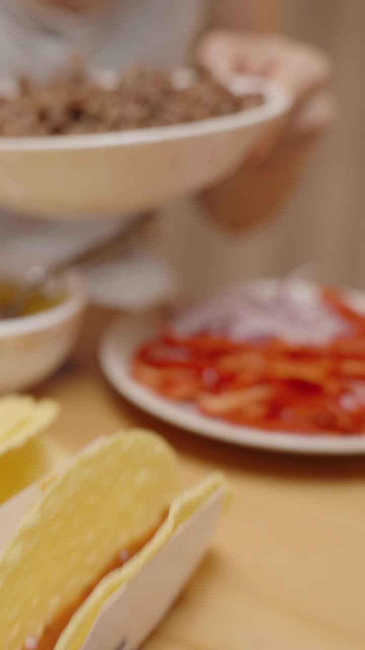 垂直视频。一名妇女在玉米饼壳里加入碎肉，准备美味的自制玉米饼。视频下载