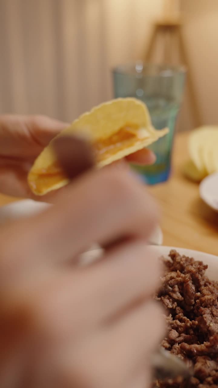 垂直视频。一个人用磨碎的肉填满玉米饼壳，用叉子加配料，在桌子上放上各种各样的配料。视频下载