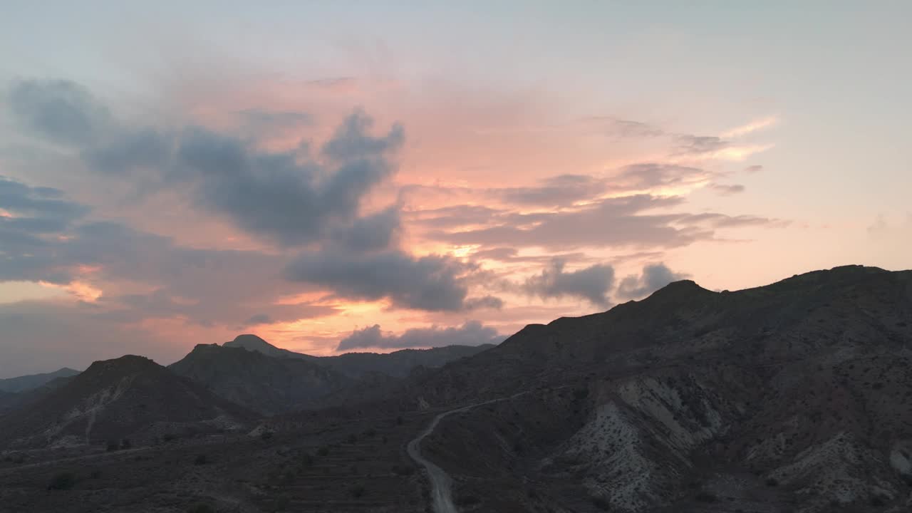 空中飞行。夕阳下，粉红色和橙色的云在山脉上移动。鸟瞰美丽的山景视频下载