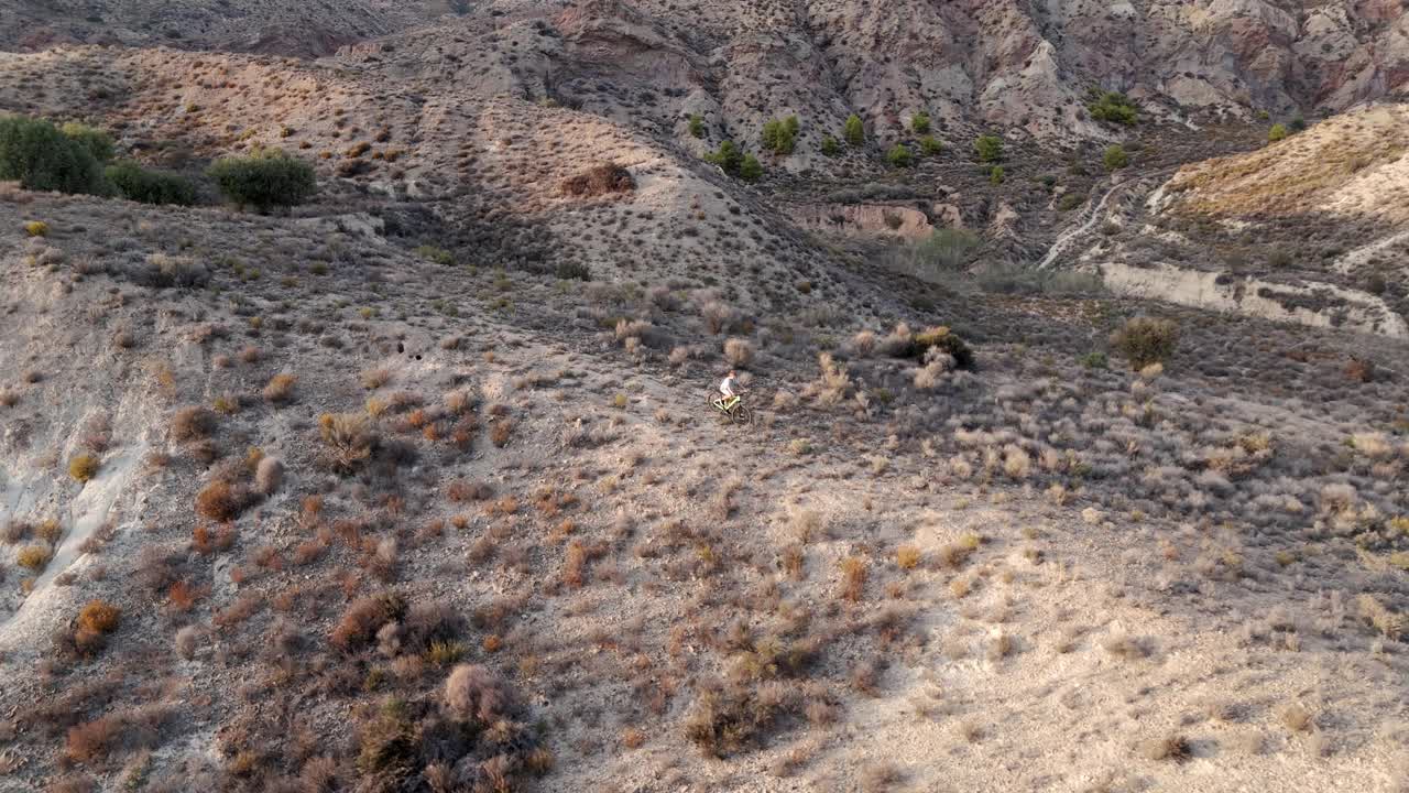 空中飞行。无人机拍的电影:在沙漠环境中，骑自行车的人在山路上爬山。鸟瞰美丽的山景视频下载