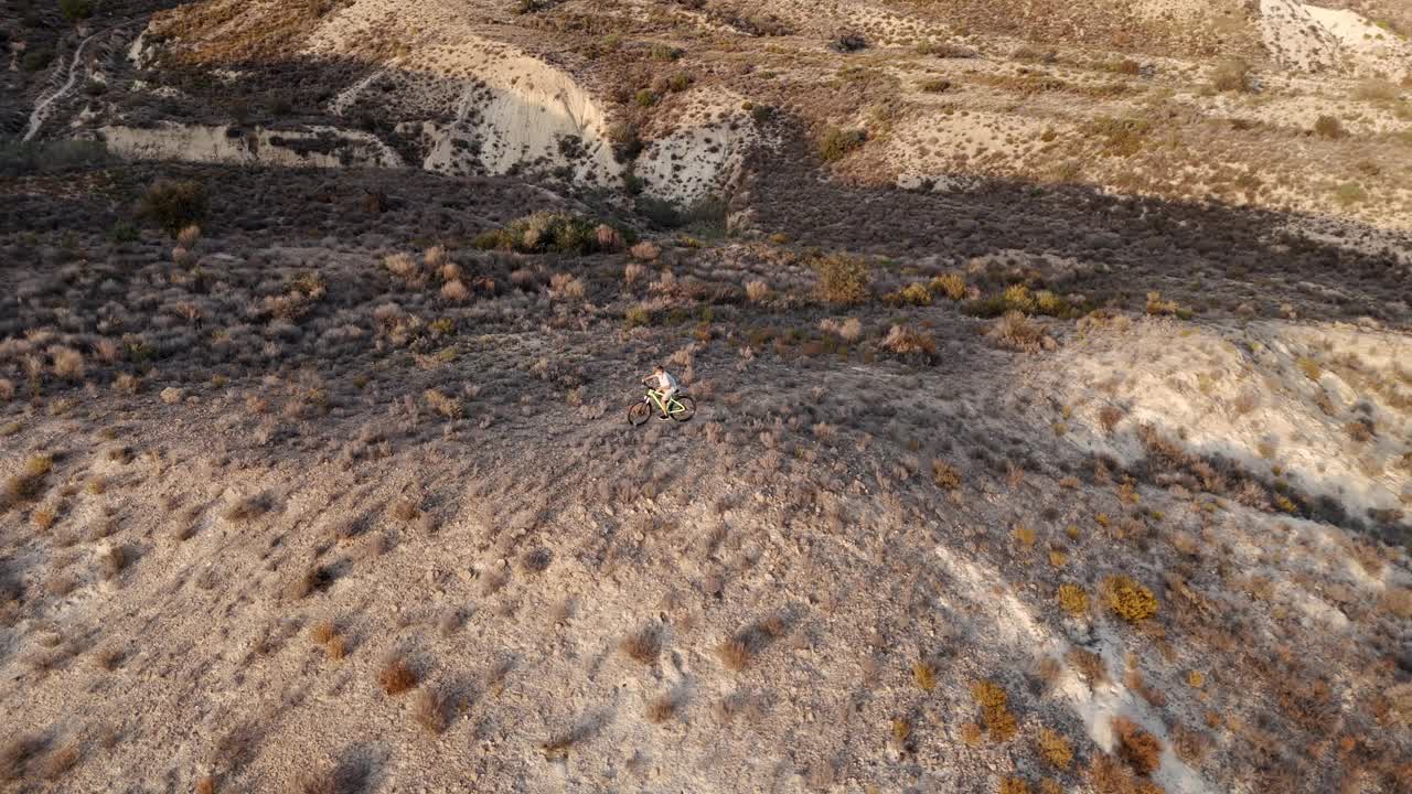 空中飞行。无人机电影镜头骑自行车的人沿着山脊线在多山的沙漠地区。鸟瞰美丽的山景视频下载