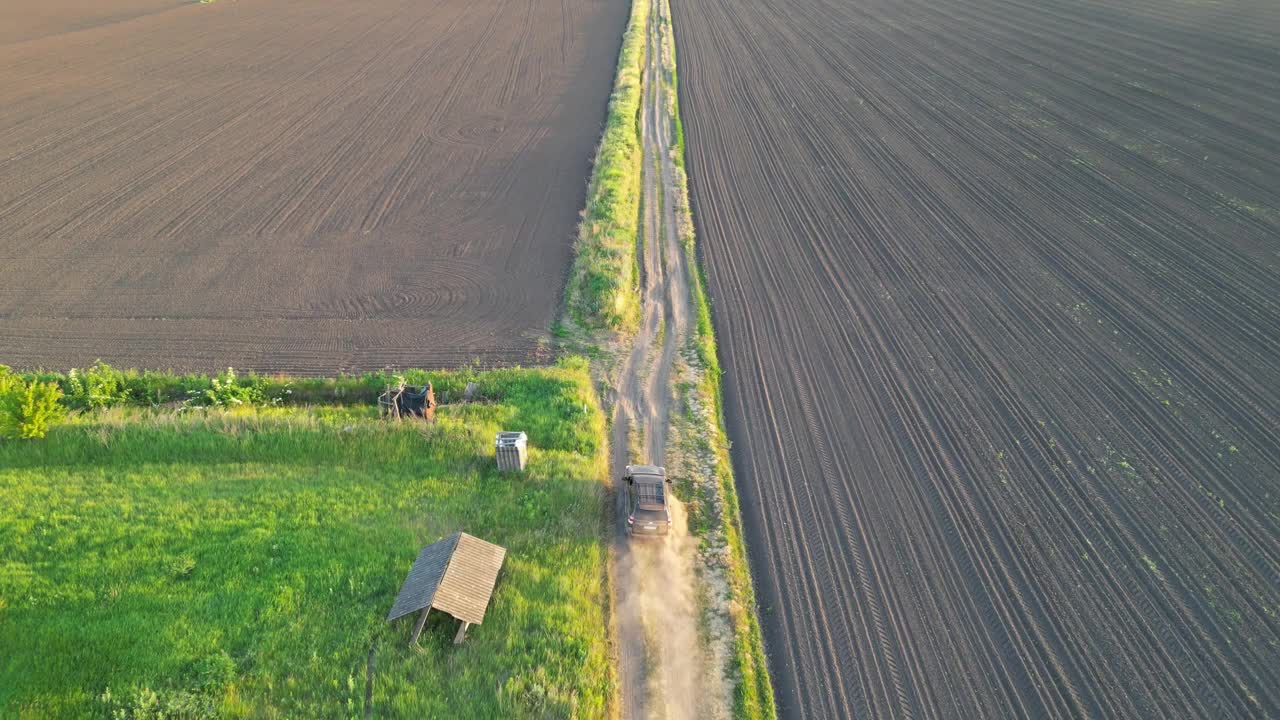 一辆拖拉机在农田里的土路上行驶的鸟瞰图。从上面可以看到拖拉机沿着绿草和棕色田野的道路行驶视频下载