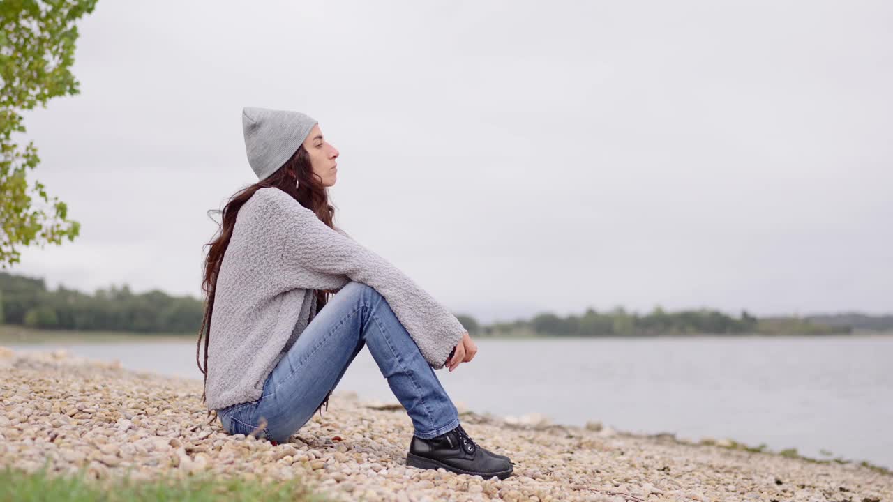 一个忧郁的女人坐在湖边。视频下载