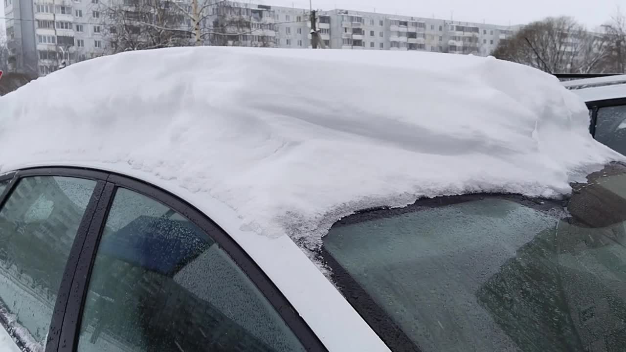 湿雪落在车顶上。冬天来了。防腐蚀和防盐保护车辆。清除汽车上的冰。城市里下雪了。霜冻寒冷的天气，暴风雪，暴风雪。开车。有雾的玻璃。视频下载