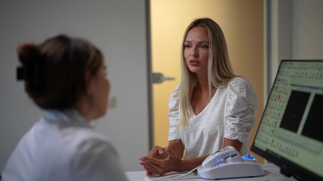 严肃的金发女子在诊所向医生抱怨健康问题。女医生解释病人治疗的后视图视频下载