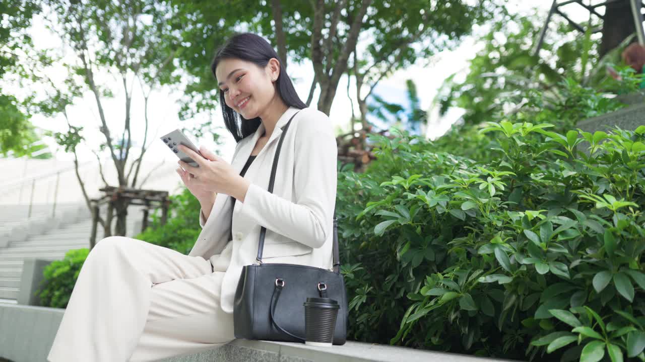 一位身穿白色西装的亚洲女商人用电话与客户沟通。位于办公室花园区域视频下载