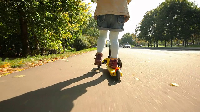 小女孩骑着黄色的踏板车在人行道上兜风。跟踪拍摄。视频素材