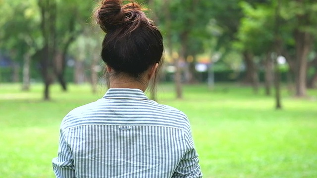 年轻的亚洲女孩转身在公园玩平板电脑视频下载