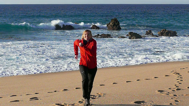 女人在海滩上跑步，海浪在背景，慢动作视频素材