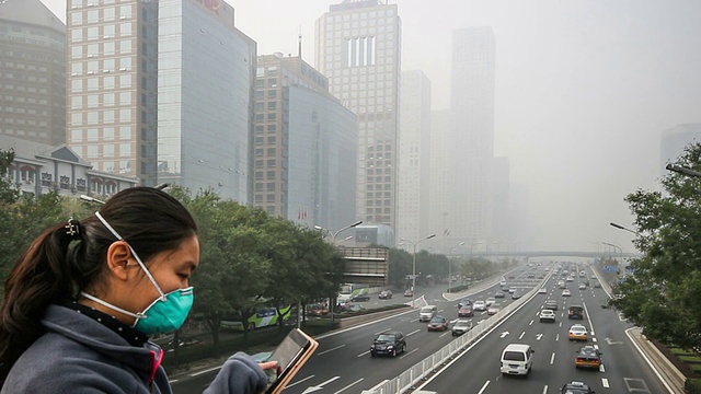 中国北京，2014年10月25日:中国北京，在恶劣的天气里，一位戴口罩的女士在国贸CBD的建筑上拍照视频素材