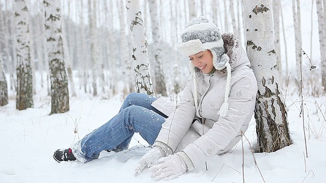 年轻美丽的女子雕刻雪球，倚着桦树坐着视频素材