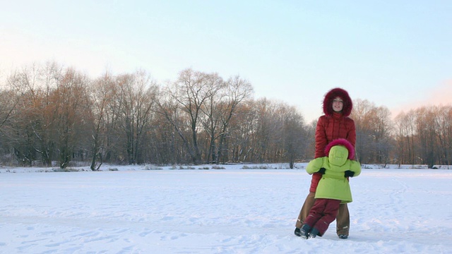 母亲和小女儿在冬天的雪地里旋转着视频素材