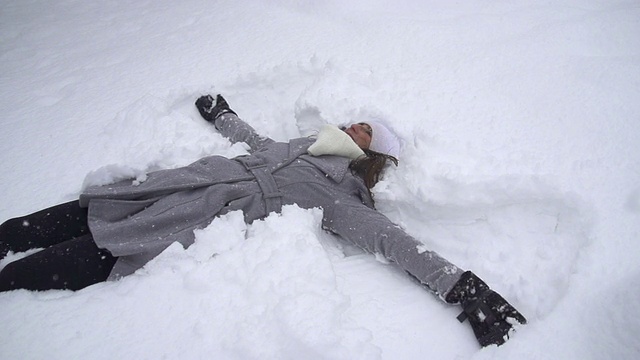 慢镜头:年轻女子在堆雪天使视频素材