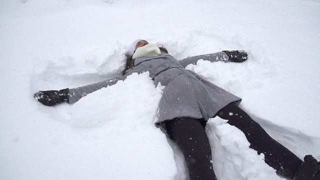 慢镜头:年轻女子在堆雪天使视频素材